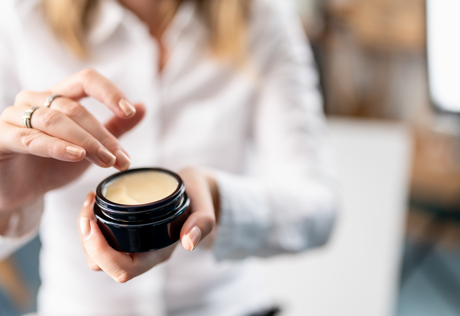 Close-up of a woman using a premium skincare cream from a dark Miron glass jar, highlighting product freshness and sustainable packaging.